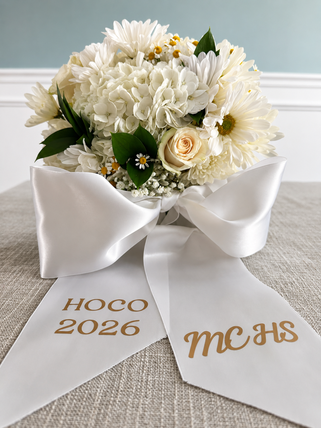 White hydrangea and cream rose homecoming bouquet with a printed school sash